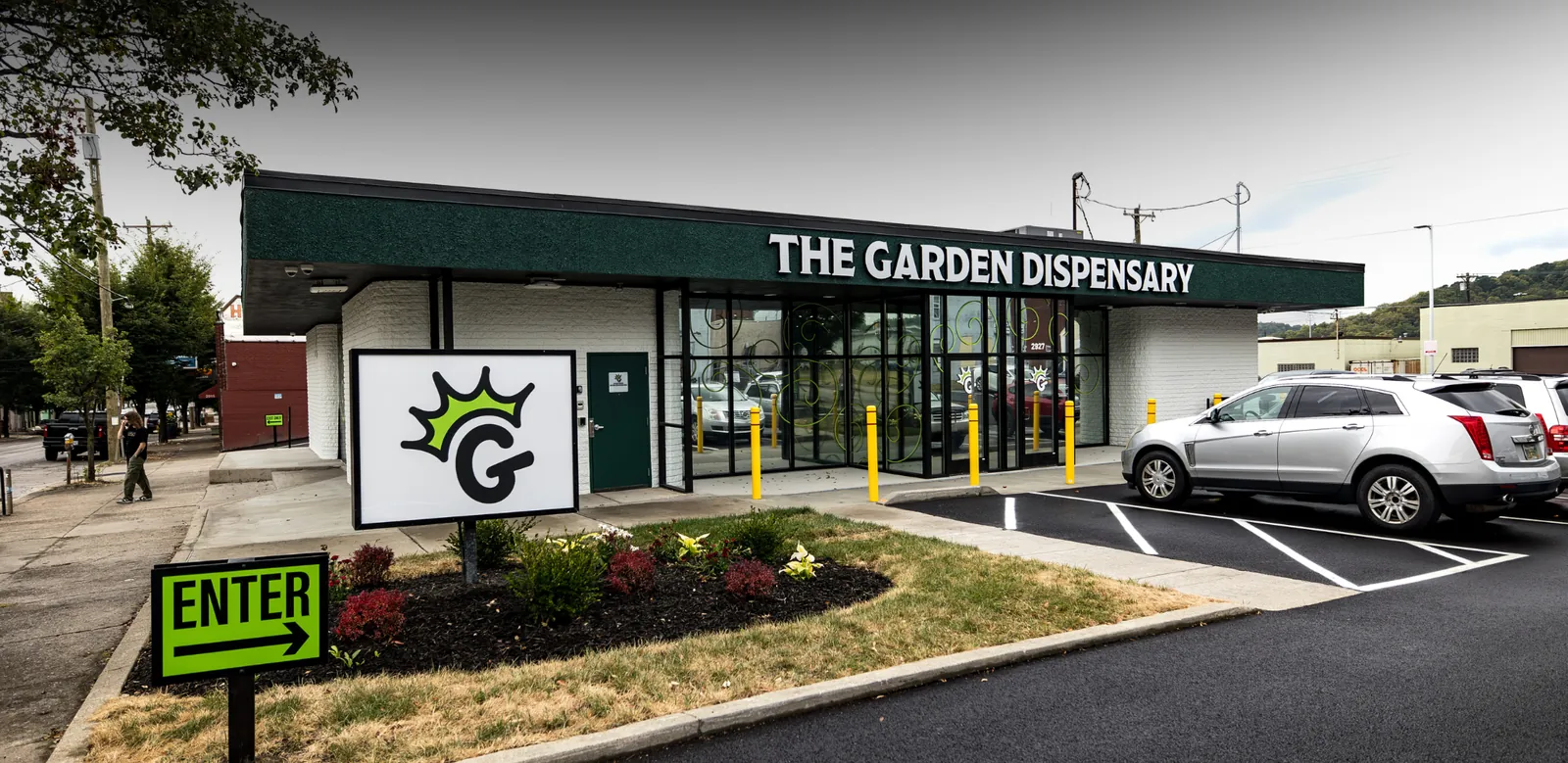 Street view of The Garden in Camp Washington, a white building striped in green, with the crowned G sign standing on the grass